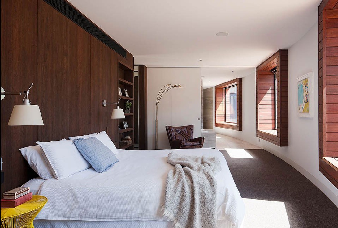 Modernt sovrum med mörk träpanelvägg som sänggavel och arkitektoniskt element.